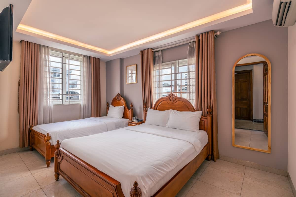 A hotel room with two wooden beds, a large mirror, and a view of the city through the windows.