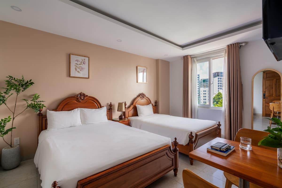A hotel room with two wooden beds, a dining table with chairs, a TV, and a large window with curtains.