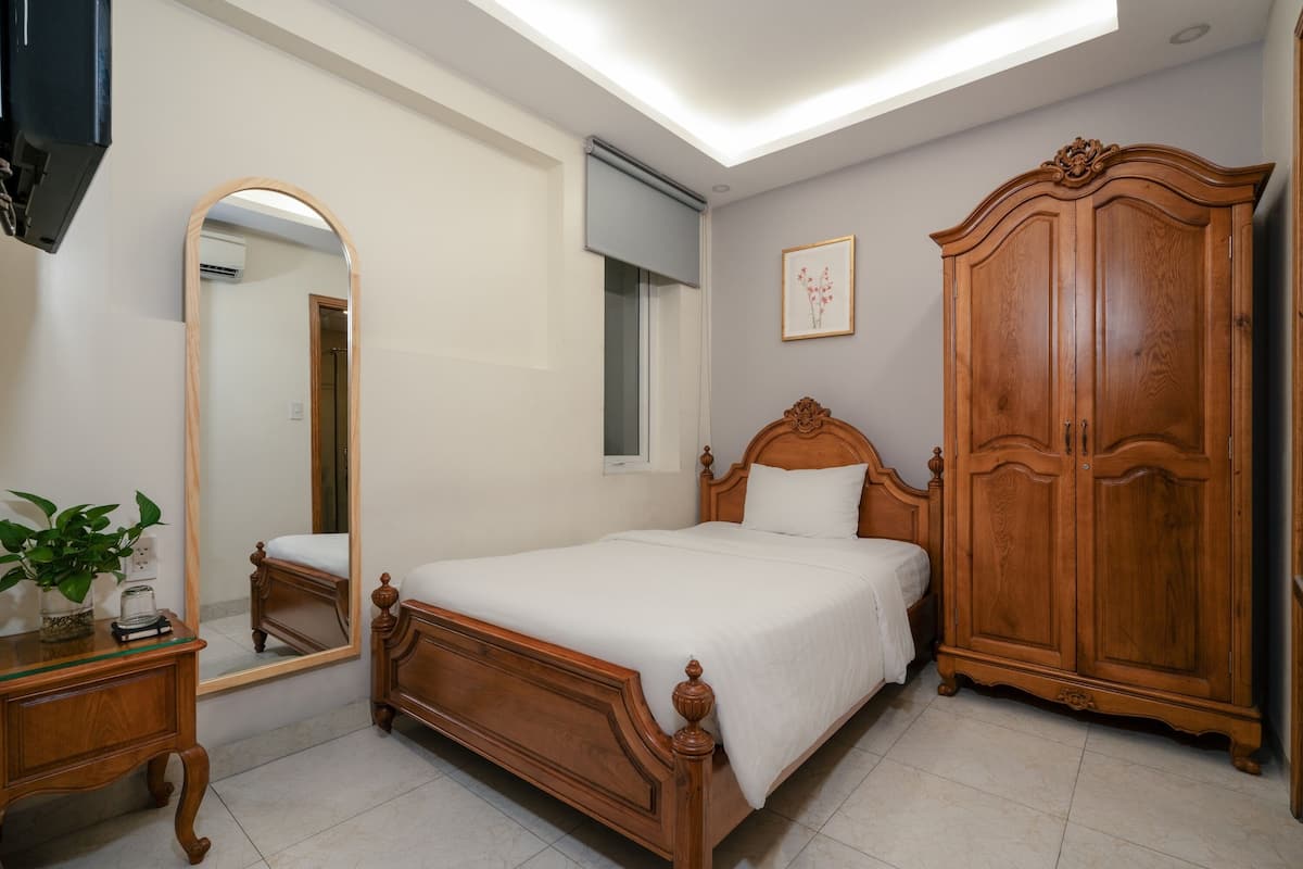 A bedroom with a wooden bed, a wardrobe, a bedside table with a plant, and a large mirror.