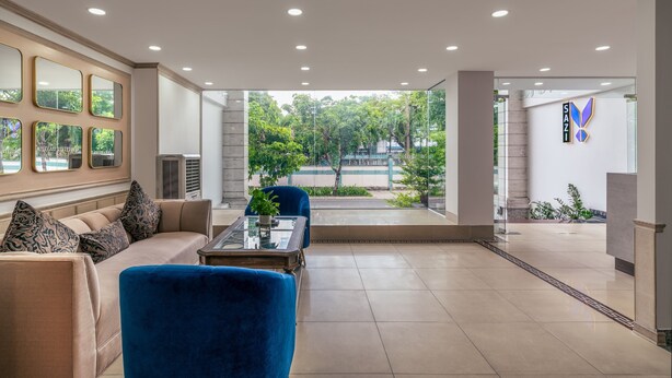 A modern lobby with a sofa, chairs, and a coffee table. There is a large window with a view of greenery and a building in the background.