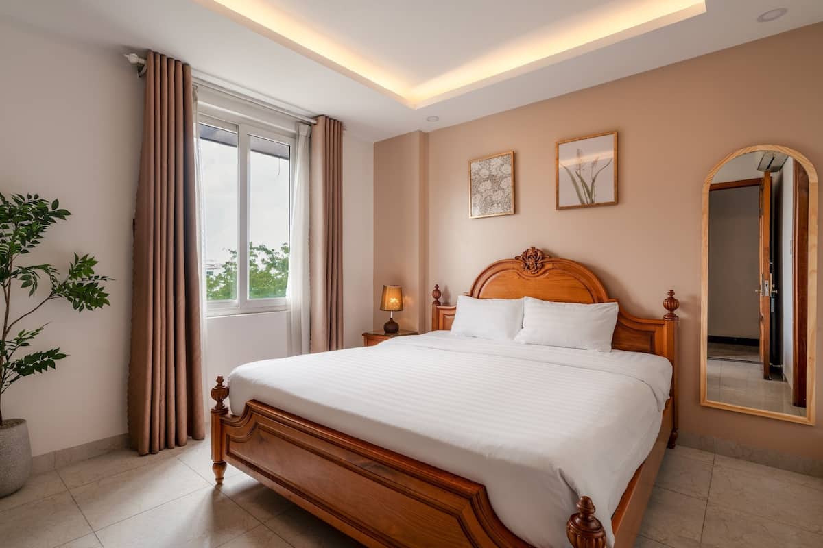 A well-lit bedroom with a large bed, a potted plant, and a window with curtains.