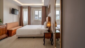 A hotel room with a bed, bedside table, lamp, TV, and a large mirror.