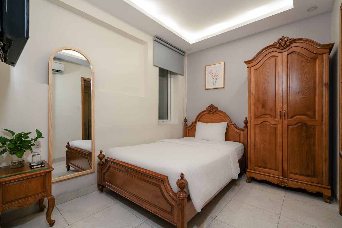 A bedroom with a wooden bed, a wardrobe, a bedside table with a plant, and a large mirror.