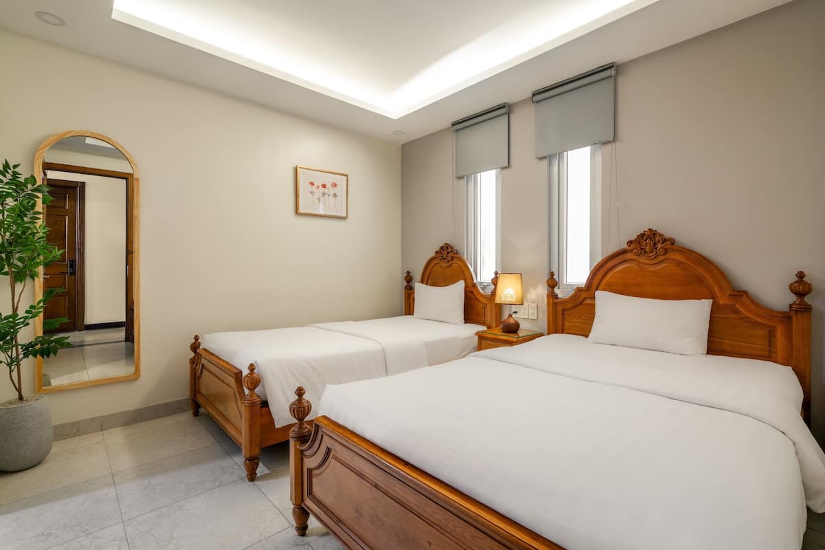 A hotel room with two wooden beds, a large mirror, a potted plant, and a framed picture on the wall.
