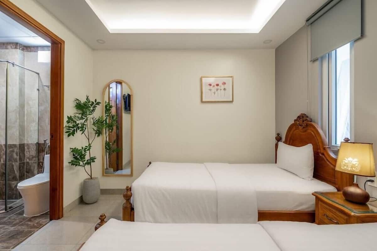 A hotel room with a bed, bedside table, lamp, potted plant, mirror, and a shower area.