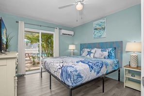 A bedroom with a bed, two bedside tables, a ceiling fan, and a view of the outside.