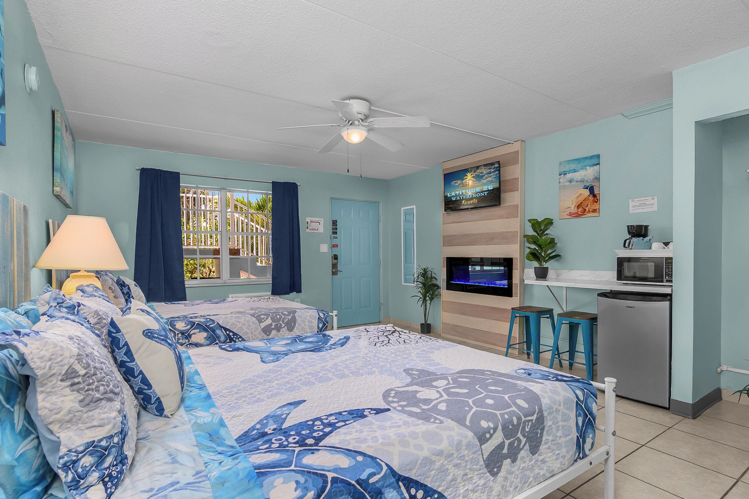 A room with a bed, a TV, a kitchenette, and a window with curtains.