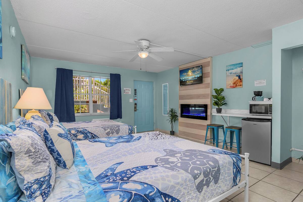 A room with a bed, a TV, a kitchenette, and a window with curtains.