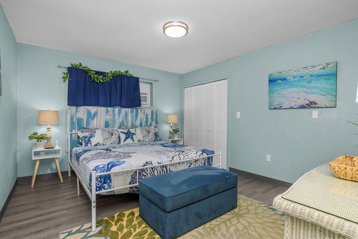A bedroom with a bed, bedside tables, a window with curtains, a wall painting, and a door.
