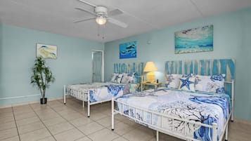 A bedroom with two beds, a ceiling fan, a potted plant, and artwork on the walls.