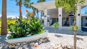 A covered outdoor area with a boat-shaped planter filled with plants, surrounded by rocks and palm trees. - Latitude 26 Waterfront Boutique Resort - Fort Myers Beach (Fort Myers Beach)