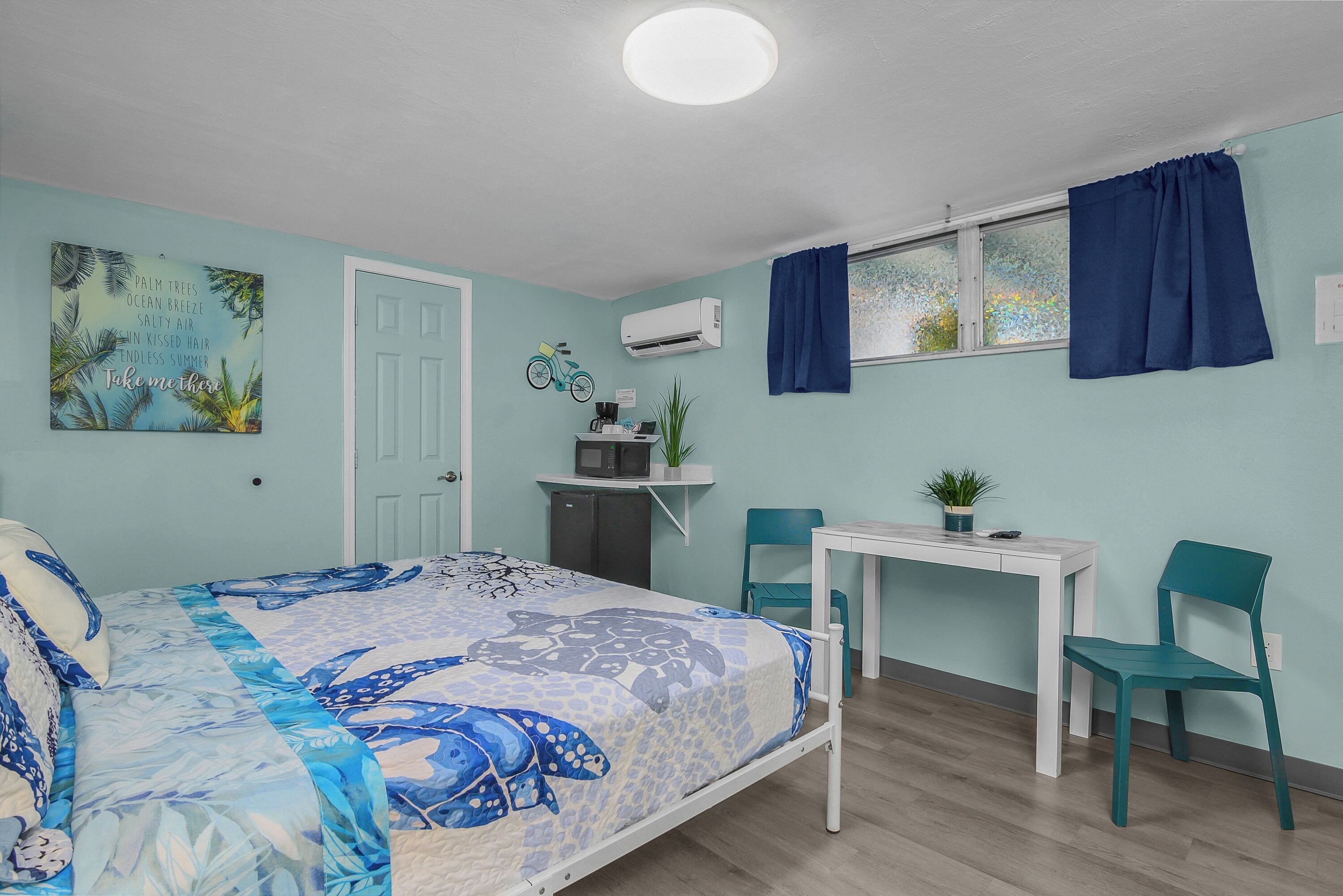 Une chambre à coucher comprenant un lit, un bureau, deux chaises, un climatiseur et une fenêtre avec des rideaux.