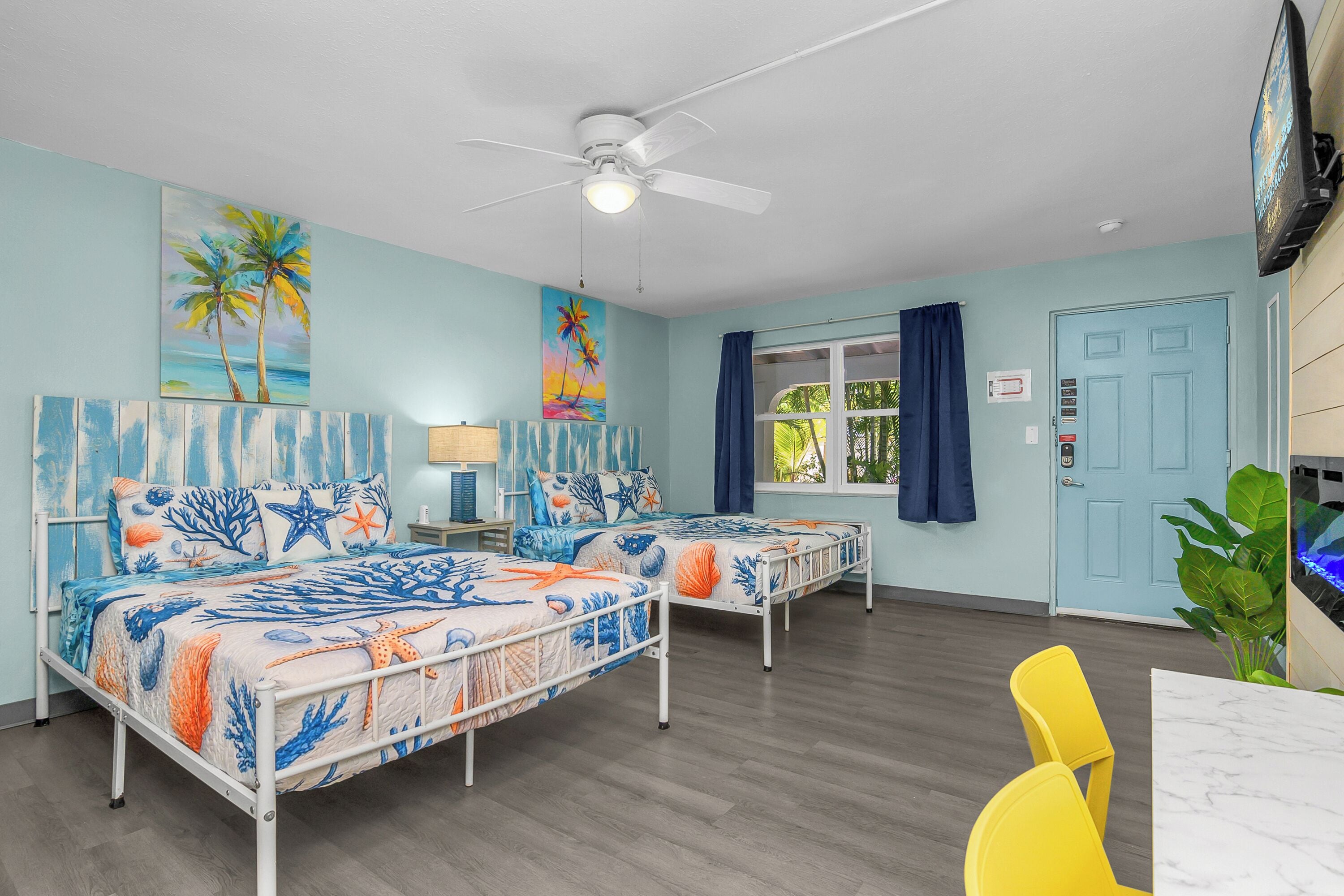 A room with two beds, a ceiling fan, a TV, and a window with curtains.