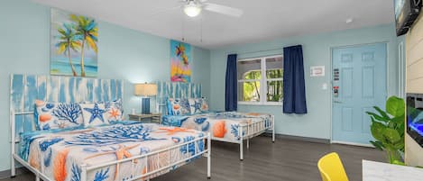 A room with two beds, a ceiling fan, a TV, and a window with curtains.
