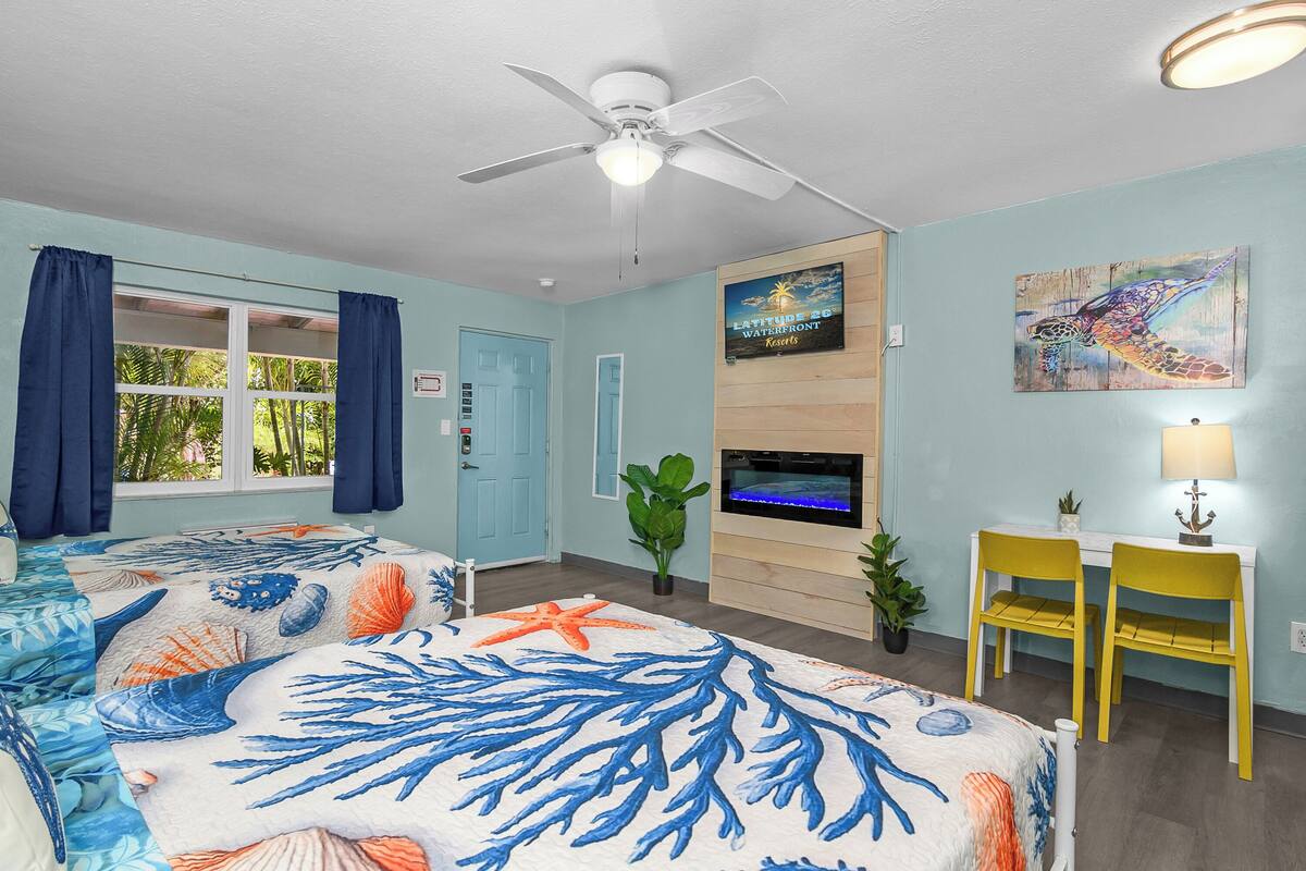 A room with a bed, a desk, chairs, a TV, and a ceiling fan.