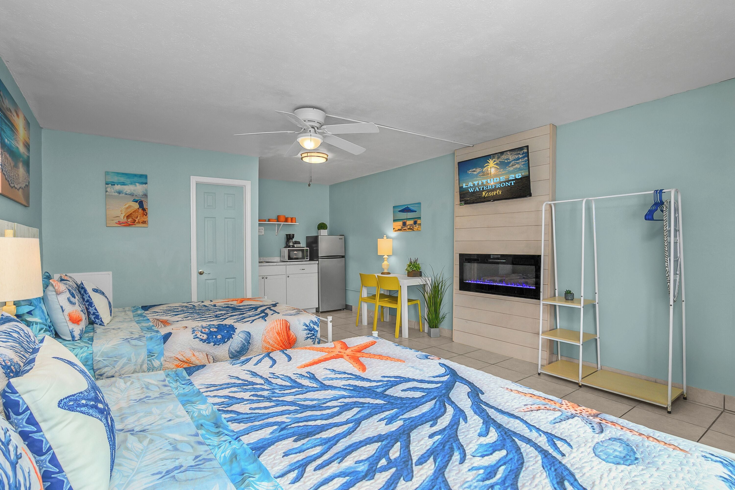 A room with a bed, a ceiling fan, a kitchen area, and a mounted TV.