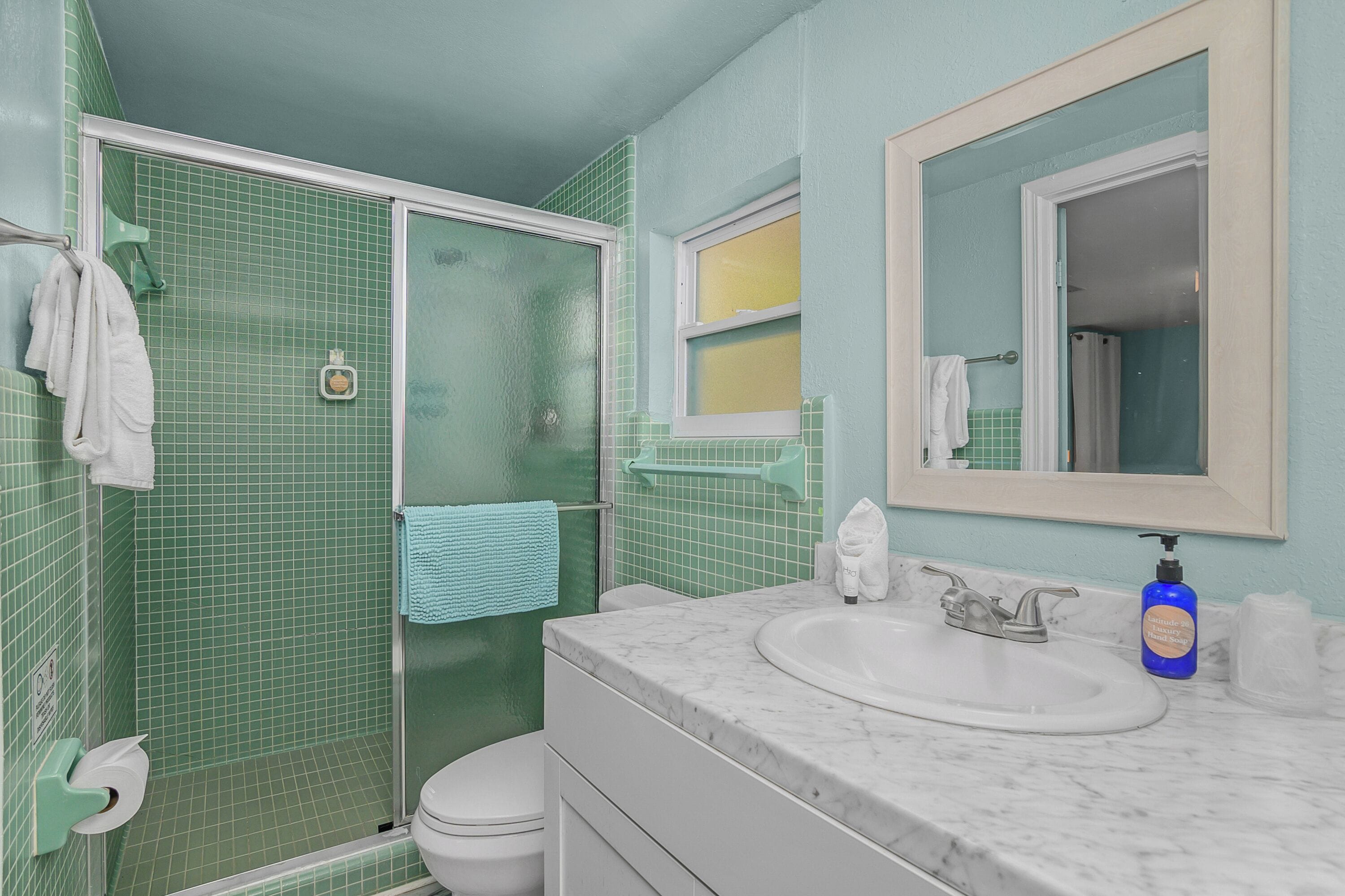 A bathroom with a shower, toilet, sink, and a mirror.