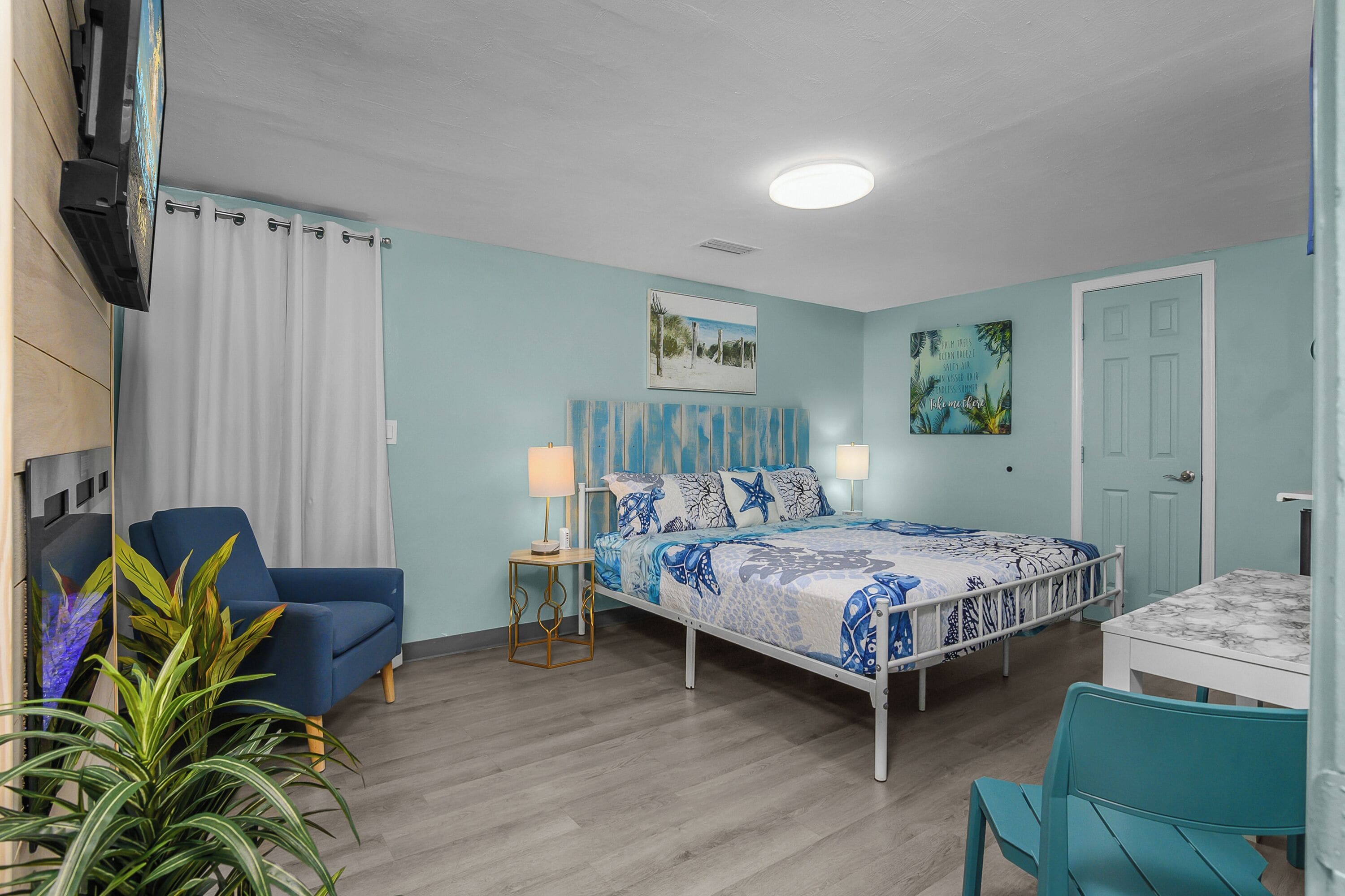 Une chambre avec un lit, une chaise, une table, un téléviseur et une plante.