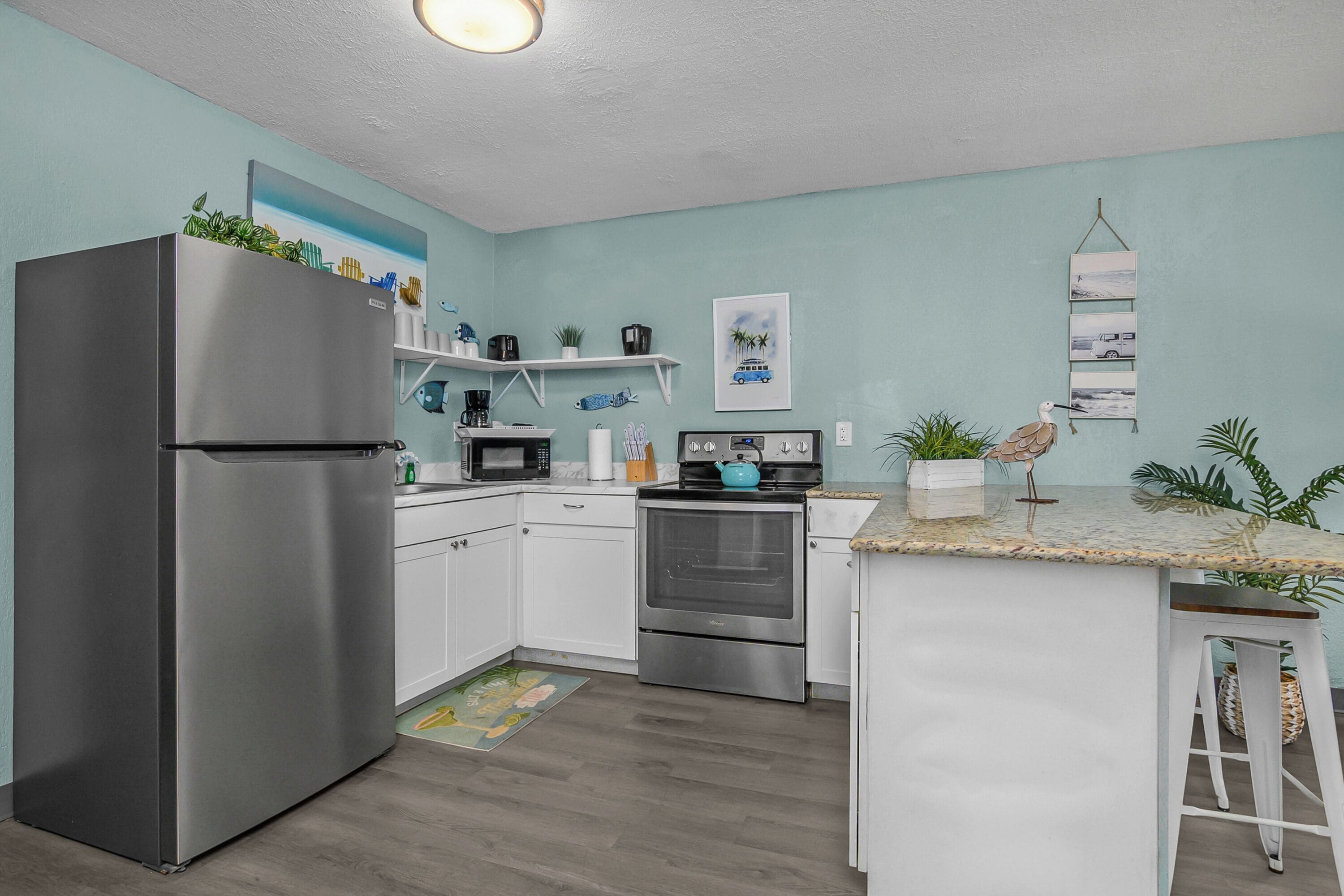 Una cocina moderna con gabinetes blancos, electrodomésticos de acero inoxidable y una pared de acento color turquesa.
