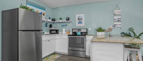 Una cocina moderna con gabinetes blancos, electrodomésticos de acero inoxidable y una pared de acento color turquesa.