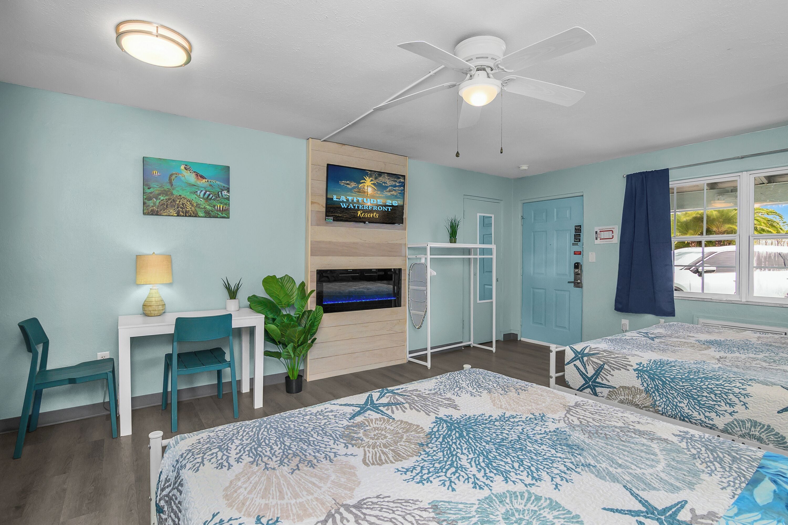 A bedroom with a bed, a desk, a chair, a ceiling fan, a TV, and a window with curtains.