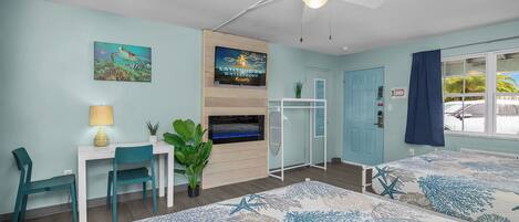 A bedroom with a bed, a desk, a chair, a ceiling fan, a TV, and a window with curtains.