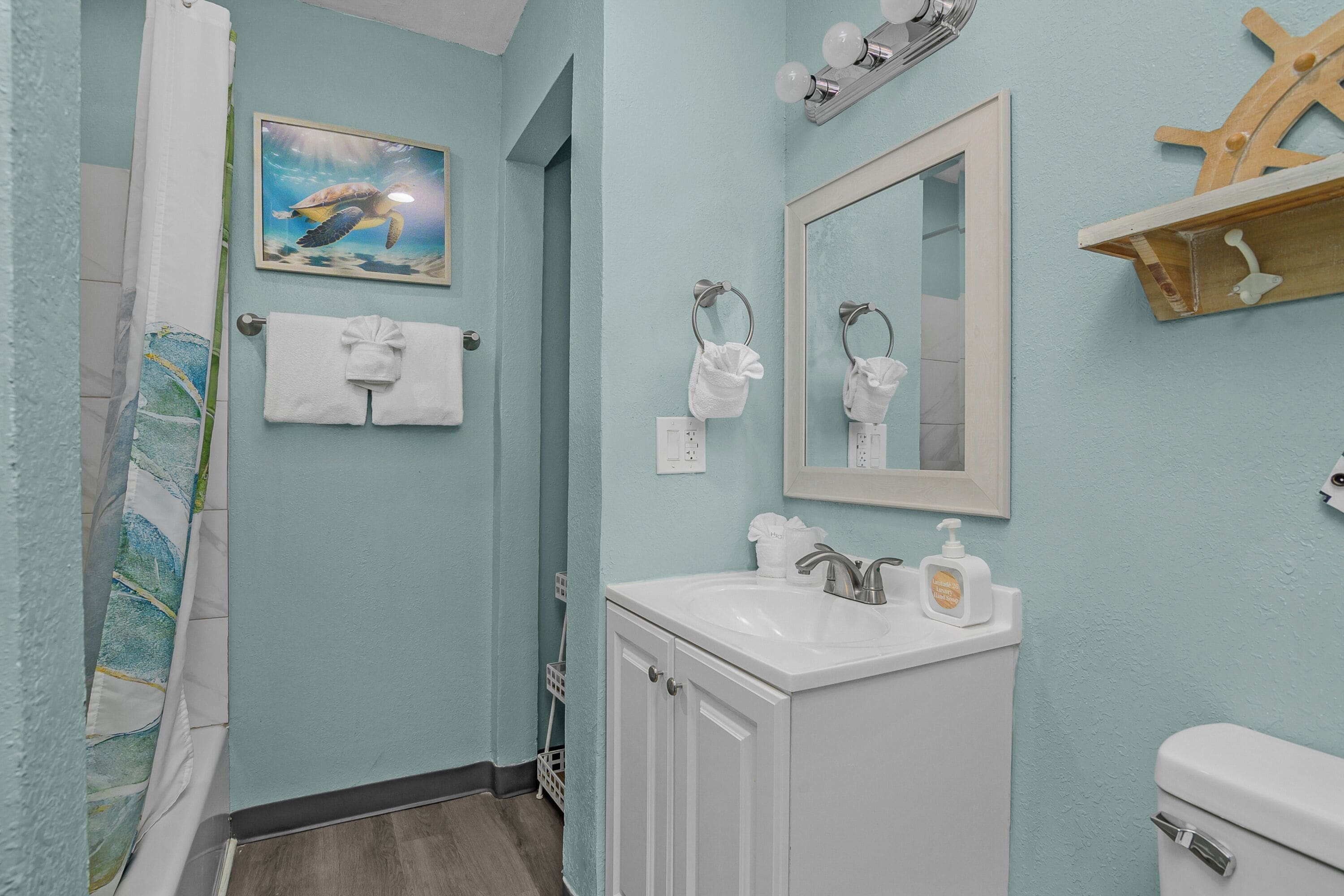 A bathroom with a light blue wall, a white sink, a mirror, a towel rack, and a shower curtain.