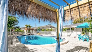 A swimming pool with a thatched roof overhead, surrounded by lounge chairs and a covered patio area. - Latitude 26 Waterfront Boutique Resort - Fort Myers Beach (Fort Myers Beach)