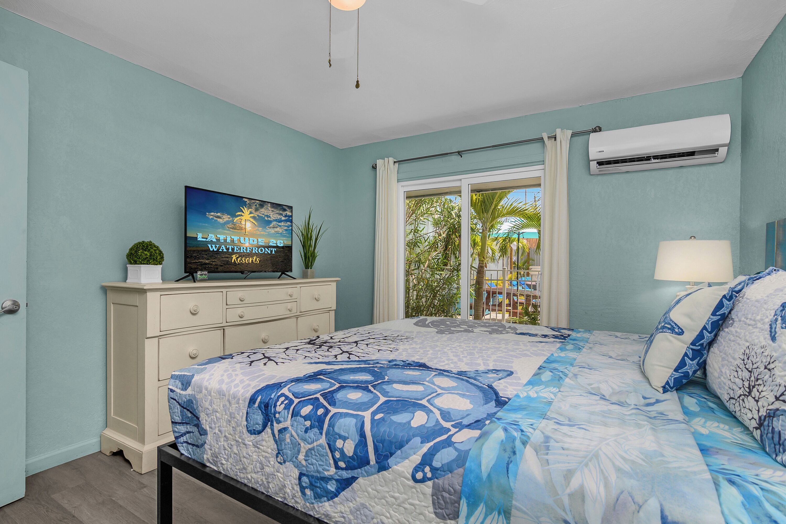 A bedroom with a bed, a television, a window with curtains, and an air conditioning unit.