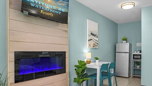 A room with a large aquarium, a dining table with chairs, a refrigerator, and a wall-mounted TV displaying a resort advertisement. - Latitude 26 Waterfront Boutique Resort - Fort Myers Beach (Fort Myers Beach)