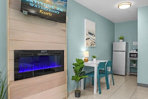 Et værelse med et stort akvarium, et spisebord med stole, et køleskab og et vægmonteret fjernsyn, der viser reklame for et resort.