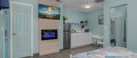 A bedroom with a bed, a ceiling fan, a TV, a refrigerator, a microwave, a sink, and a small desk.