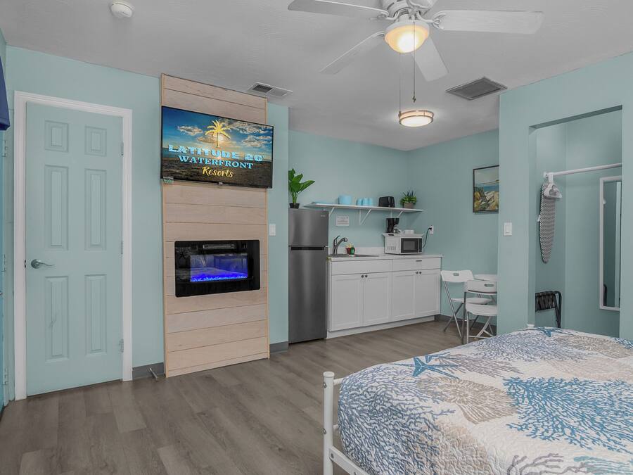 A bedroom with a bed, a ceiling fan, a TV, a refrigerator, a microwave, a sink, and a small desk.