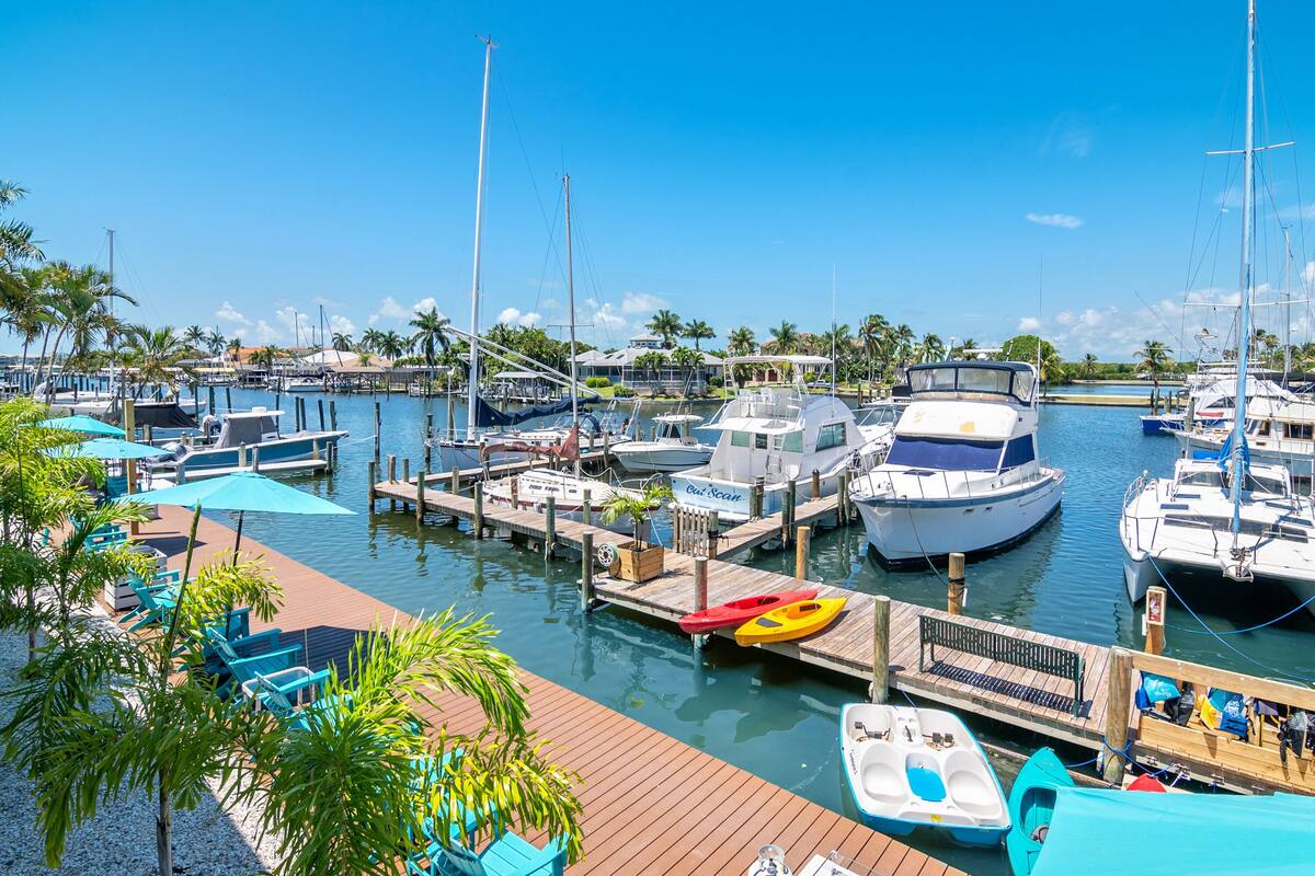 A marina with boats docked, a wooden dock, and a row of blue chairs and umbrellas.