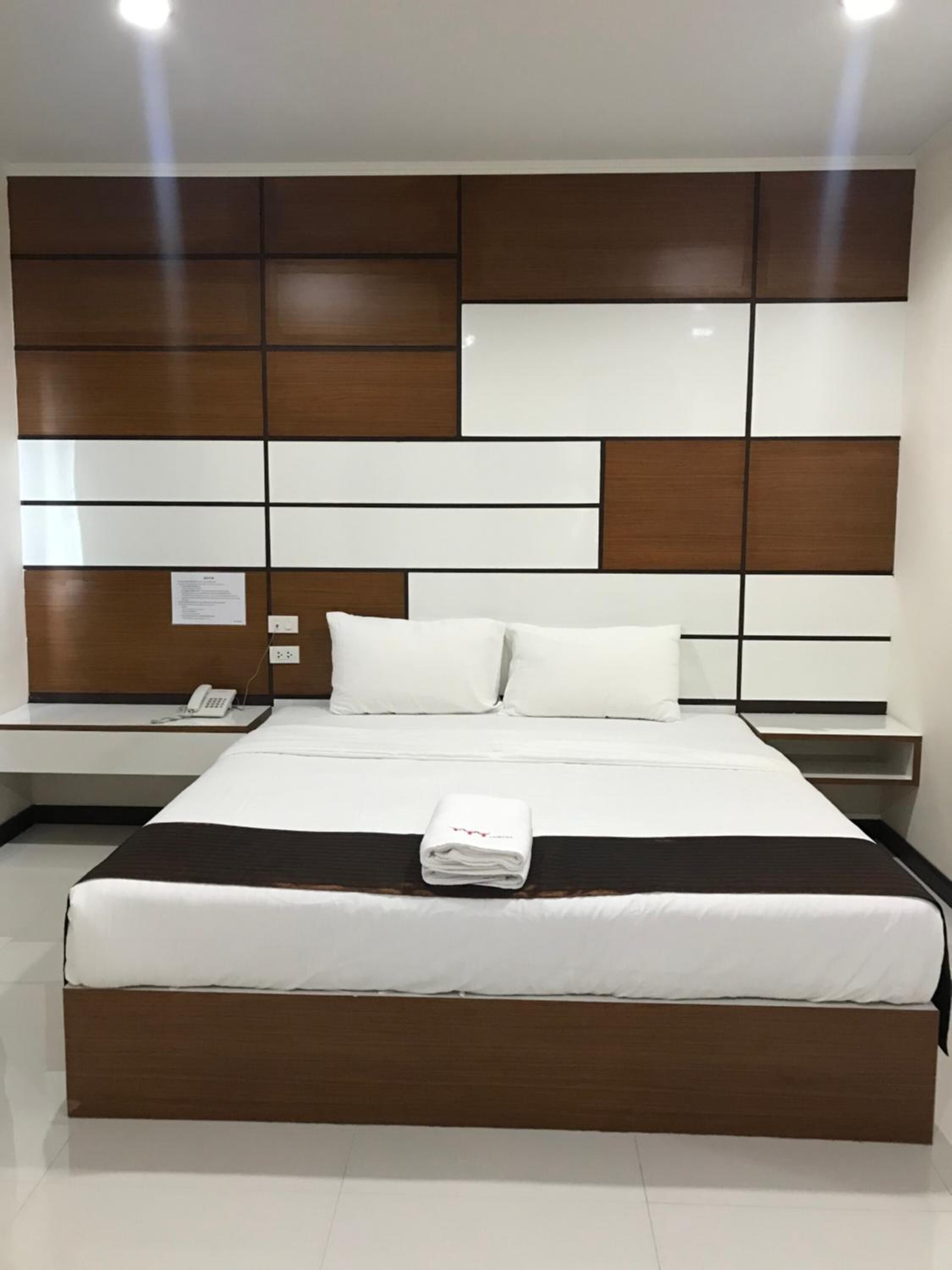 A hotel room with a large bed, a bedside table with a phone, and a wall with a geometric pattern.