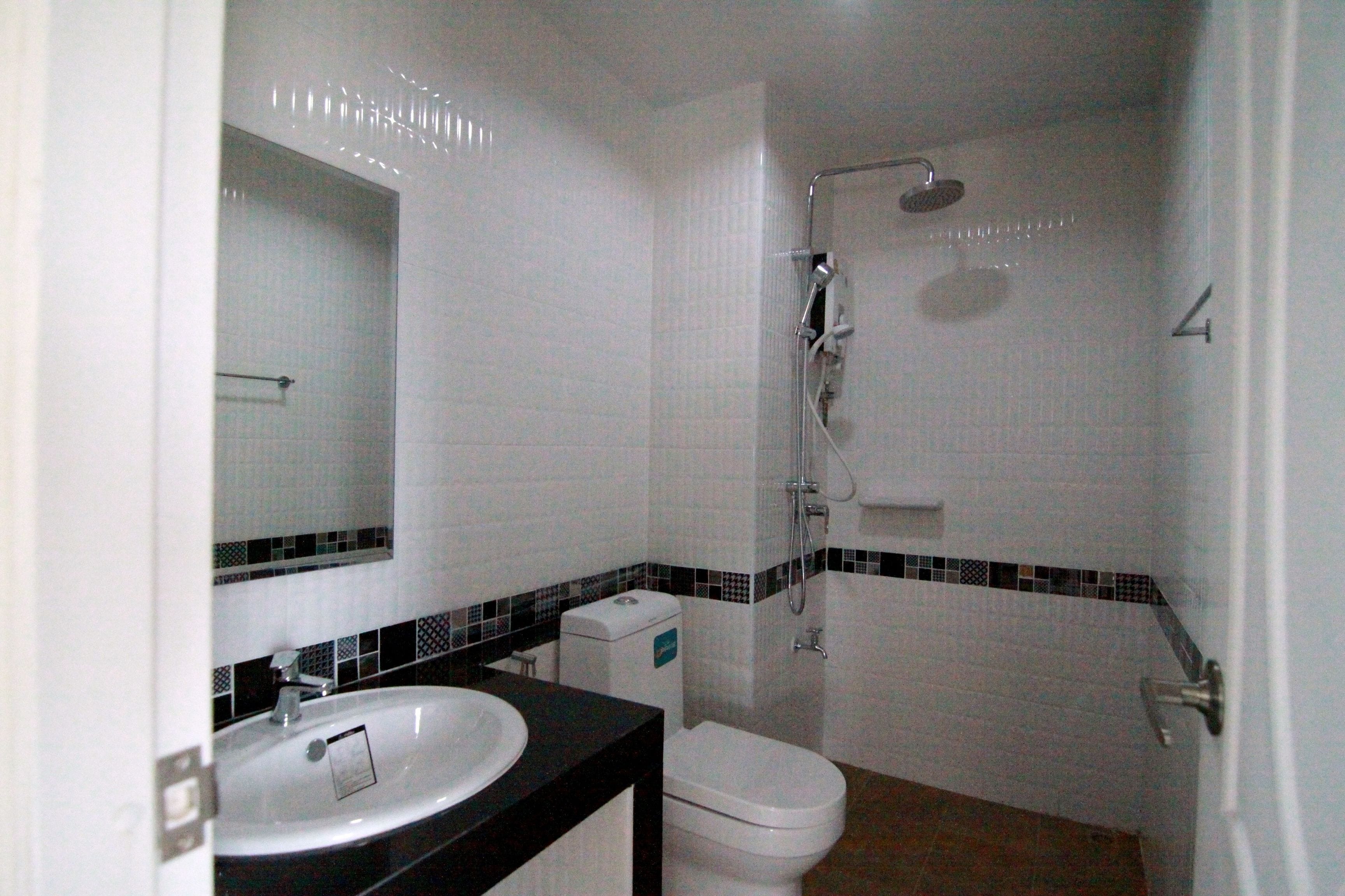 A bathroom with a white sink, black countertop, white toilet, and a shower area.
