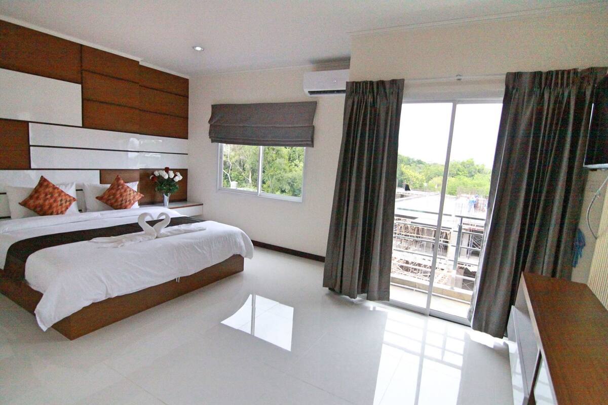 A modern hotel room with a large bed, a flat-screen TV, and a balcony with a view.