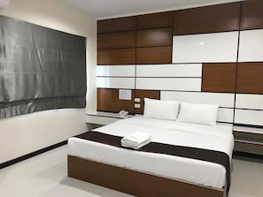 A modern hotel room with a large bed, a bedside table with a phone, and a view of the city. - TTT Hotel (Hat Yai)