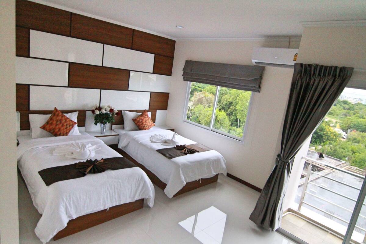 A hotel room with two beds, a large window with a view, a modern headboard, and a balcony.