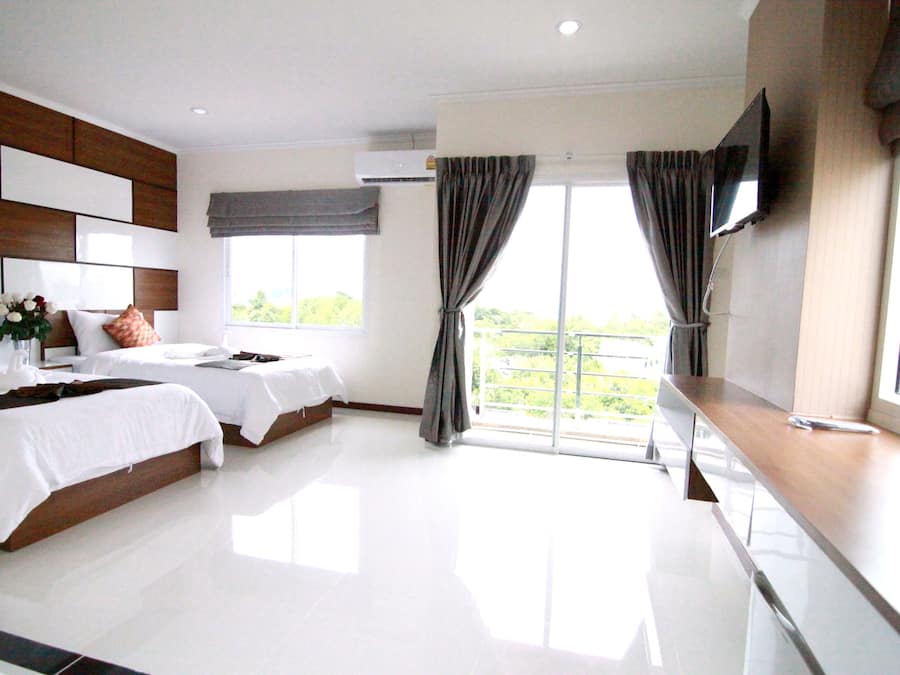 Quarto de hotel com duas camas, televisão e varanda com cortinas.