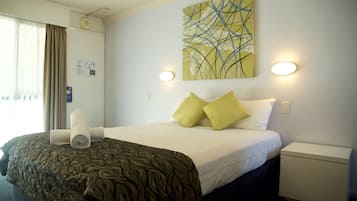 A hotel room with a neatly made bed, a bedside table, a wall-mounted artwork, and a window with curtains.