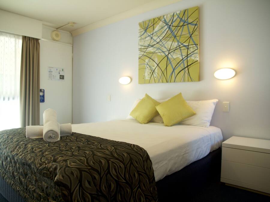 A hotel room with a neatly made bed, a bedside table, a wall-mounted artwork, and a window with curtains.