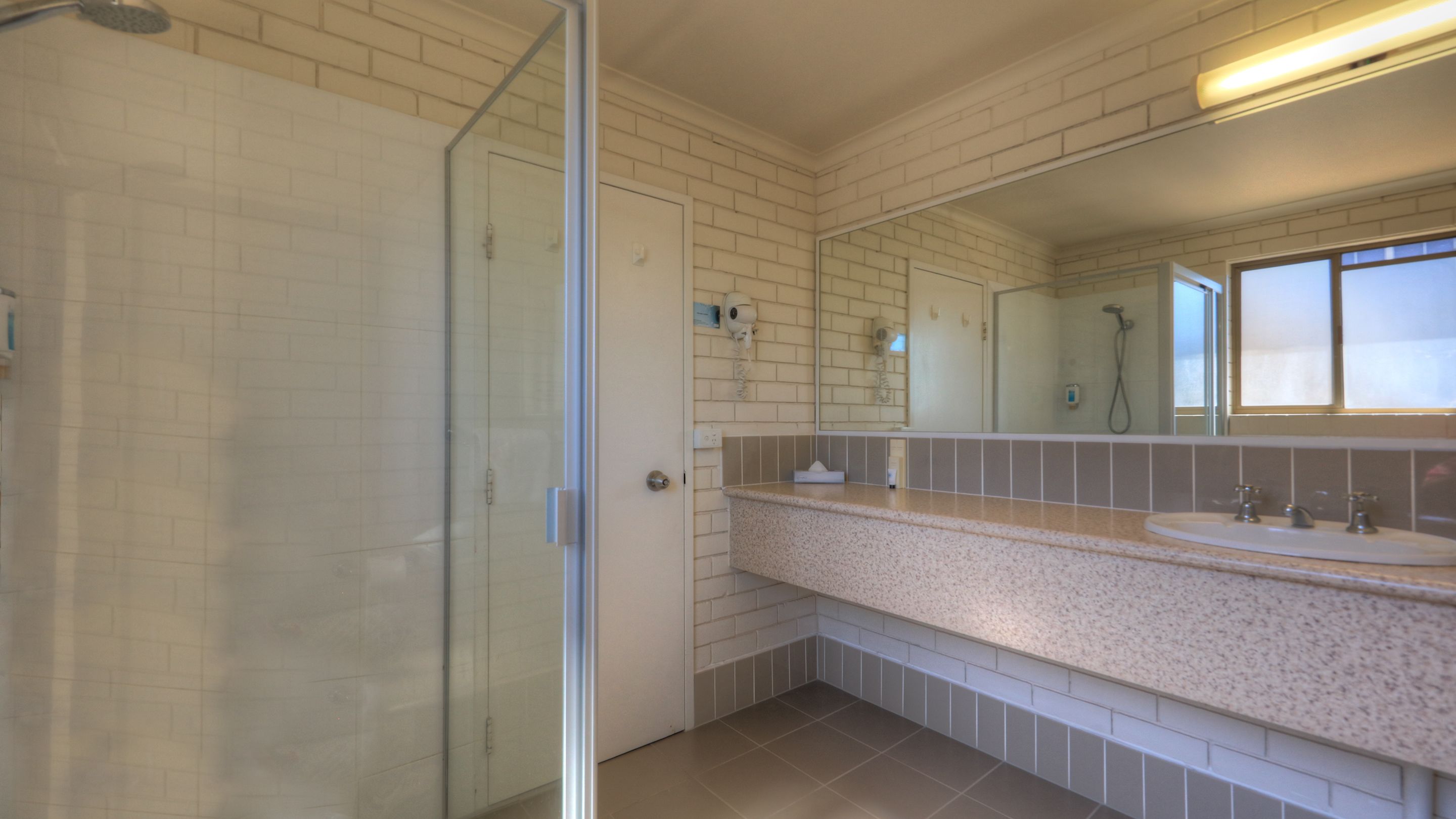 A bathroom with a glass shower door, a large mirror, and a granite countertop with a sink.