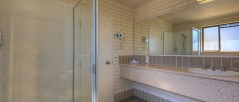 A bathroom with a glass shower door, a large mirror, and a granite countertop with a sink.
