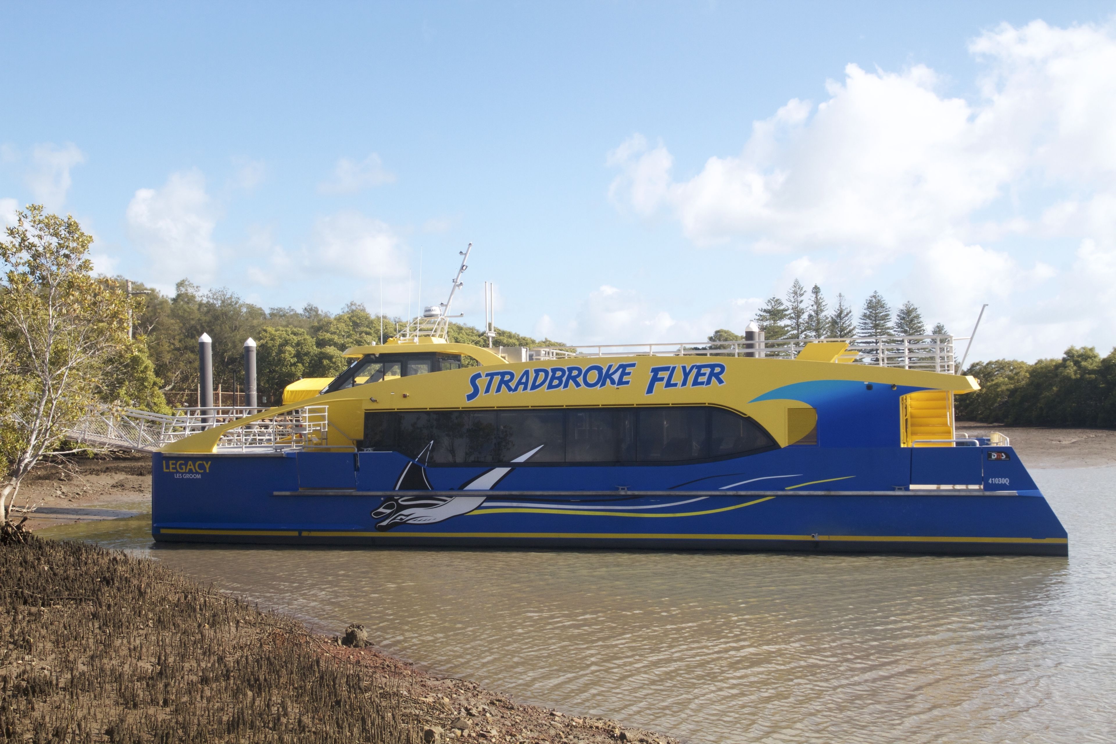 Un grand traversier aux couleurs bleu et jaune, baptisé « Stradbroke Flyer », accosta sur la rive d’une rivière.