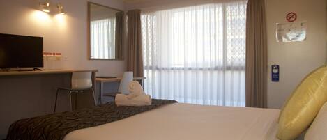 A hotel room with a bed, a desk with a television, a chair, and a window with curtains.