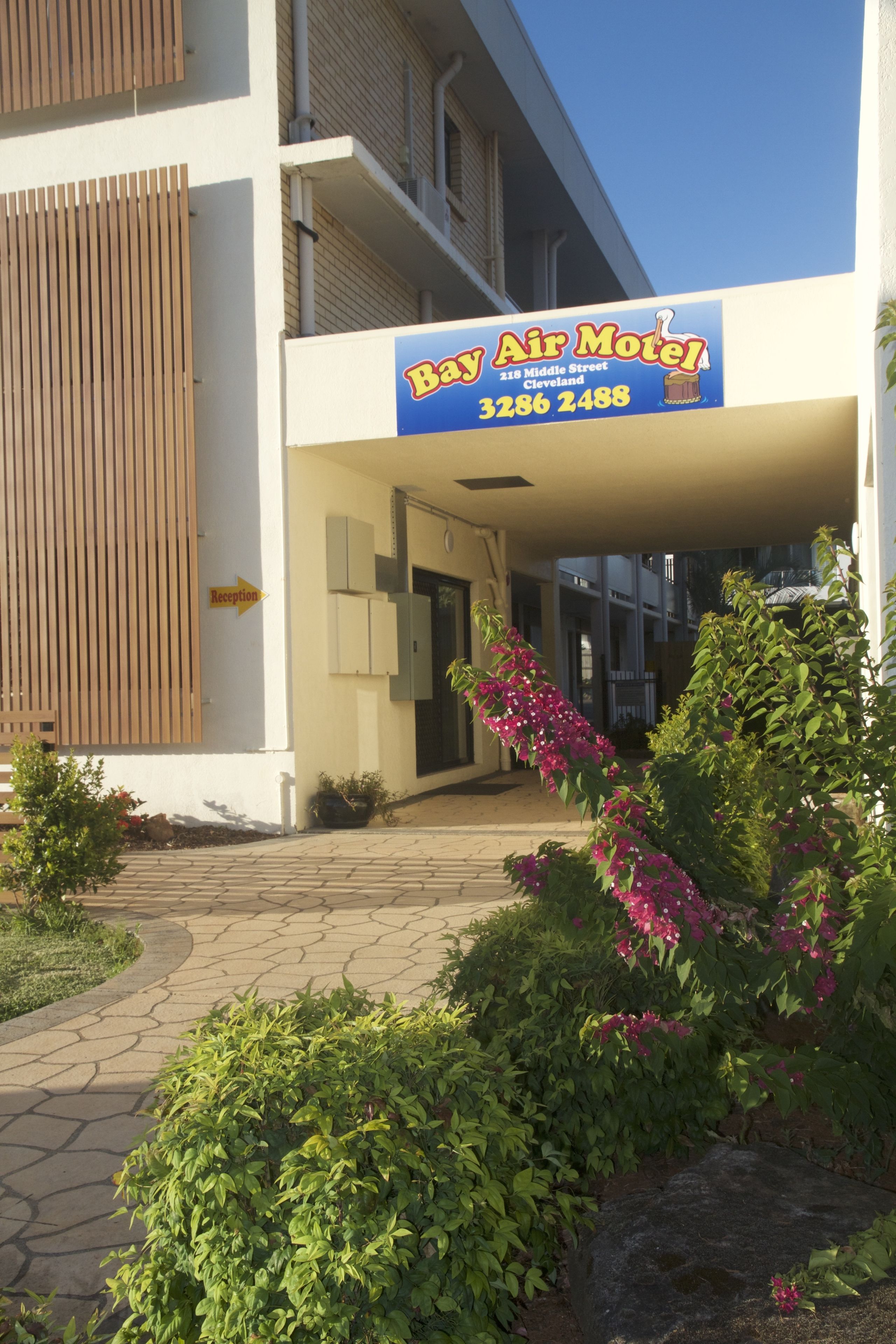 The exterior of Bay Air Motel with a reception sign, a paved walkway, and surrounding greenery.
