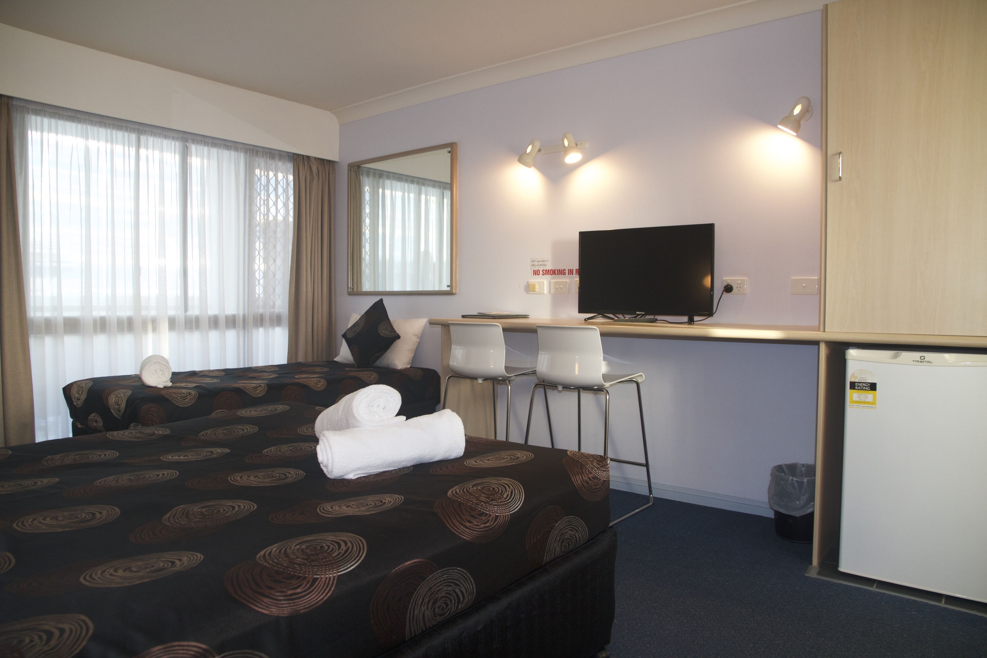 A hotel room with a large bed, a desk with a television, and a small refrigerator.