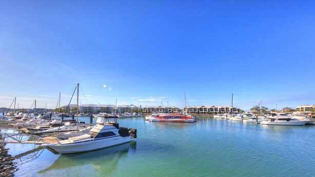 A marina with multiple boats docked, a clear blue sky, and a row of buildings in the background. - Bay Air Motel (Cleveland)