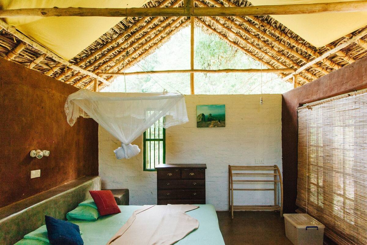 A room with a bed, a small dresser, a nightstand, a window with bars, a painting on the wall, and a mosquito net over the bed.